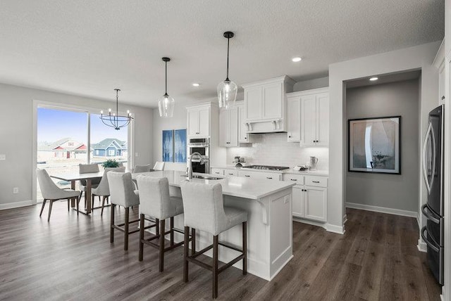 kitchen with hanging light fixtures, white cabinetry, appliances with stainless steel finishes, and an island with sink