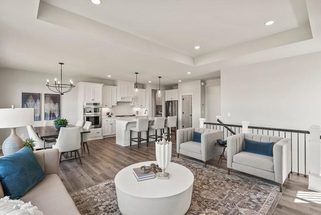 living room with an inviting chandelier, dark hardwood / wood-style flooring, a raised ceiling, and sink