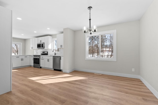 kitchen featuring white cabinetry, light wood-type flooring, stainless steel appliances, a chandelier, and pendant lighting