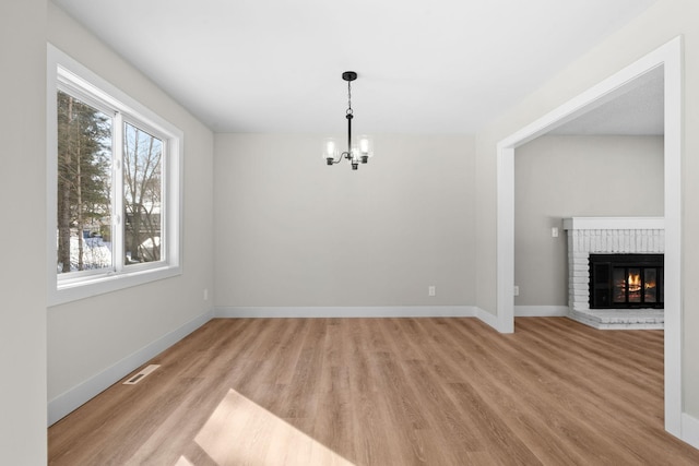 unfurnished dining area with light hardwood / wood-style flooring, an inviting chandelier, and a brick fireplace