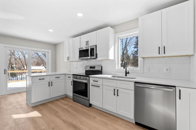 kitchen featuring appliances with stainless steel finishes, tasteful backsplash, light hardwood / wood-style floors, sink, and white cabinetry