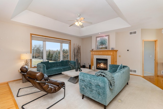 living room with wood-type flooring, ceiling fan, a fireplace, and a tray ceiling