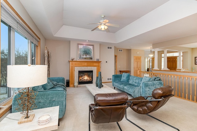 living room featuring light colored carpet, a raised ceiling, a tile fireplace, ceiling fan, and decorative columns