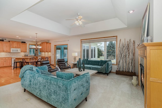 living room featuring ceiling fan with notable chandelier and a raised ceiling