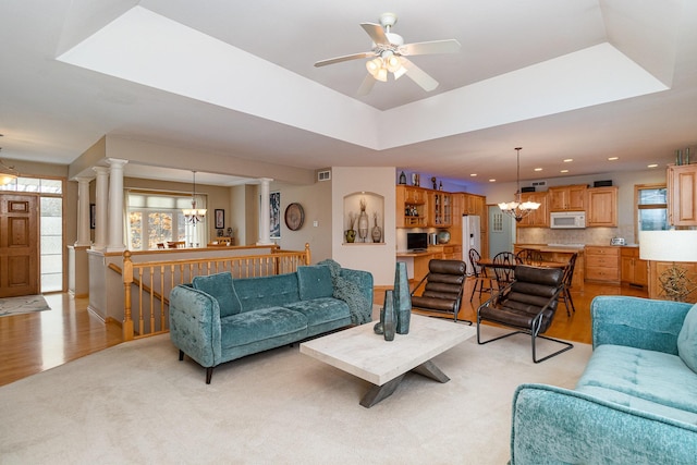 living room featuring a healthy amount of sunlight, a raised ceiling, and ornate columns