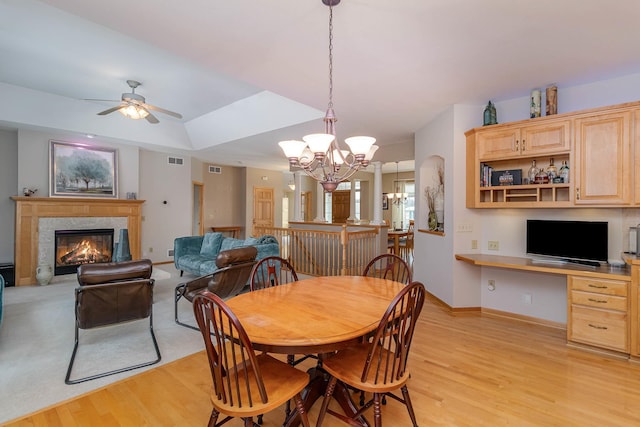 dining room featuring a high end fireplace, built in desk, light hardwood / wood-style floors, and ceiling fan with notable chandelier