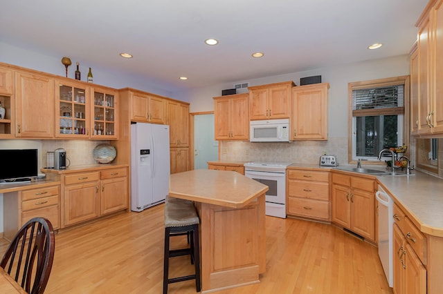 kitchen with sink, a kitchen bar, a center island, white appliances, and light hardwood / wood-style flooring