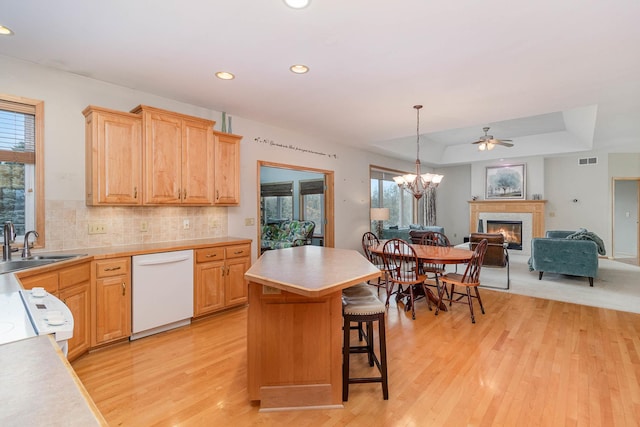 kitchen featuring a breakfast bar, a fireplace, dishwasher, a center island, and a raised ceiling