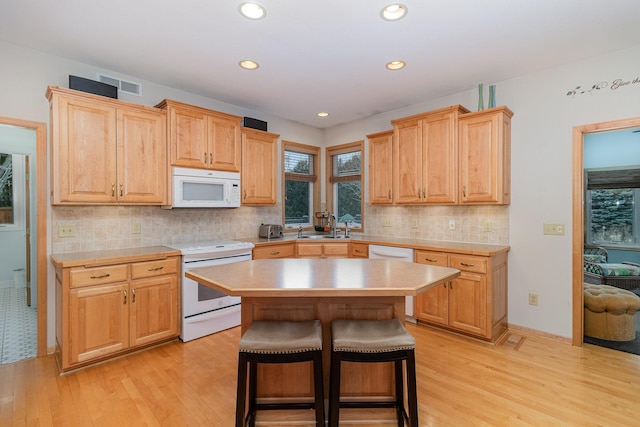 kitchen with sink, a kitchen breakfast bar, a kitchen island, a wealth of natural light, and white appliances