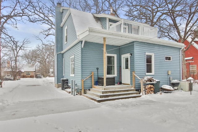 snow covered rear of property featuring central AC unit and a balcony