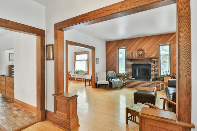 living room with a brick fireplace, beam ceiling, light hardwood / wood-style flooring, and wood walls