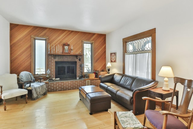 living room with a brick fireplace, wooden walls, and light hardwood / wood-style flooring