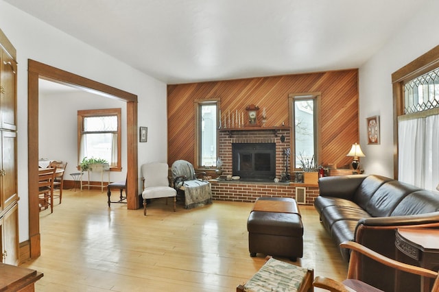 living room featuring a brick fireplace, light hardwood / wood-style floors, and wood walls