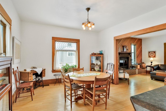 dining area with an inviting chandelier, a fireplace, and light hardwood / wood-style floors