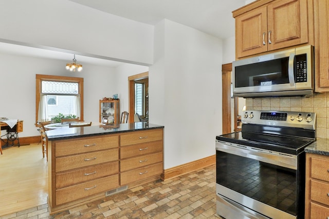 kitchen with appliances with stainless steel finishes, decorative light fixtures, a chandelier, dark stone counters, and decorative backsplash