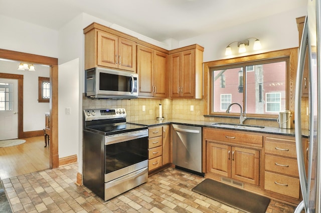 kitchen featuring sink, backsplash, dark stone counters, a notable chandelier, and stainless steel appliances