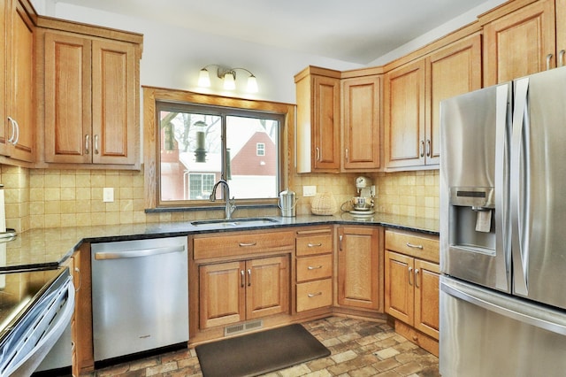 kitchen with stainless steel appliances, sink, backsplash, and dark stone counters