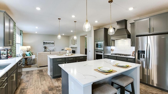 kitchen featuring premium range hood, appliances with stainless steel finishes, a kitchen breakfast bar, a kitchen island, and pendant lighting