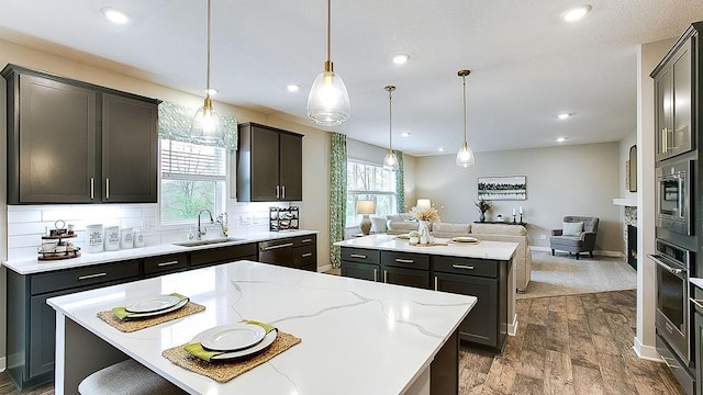 kitchen featuring appliances with stainless steel finishes, sink, hanging light fixtures, a center island, and light stone countertops