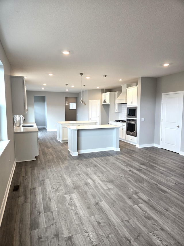 kitchen with premium range hood, a kitchen island, appliances with stainless steel finishes, pendant lighting, and sink