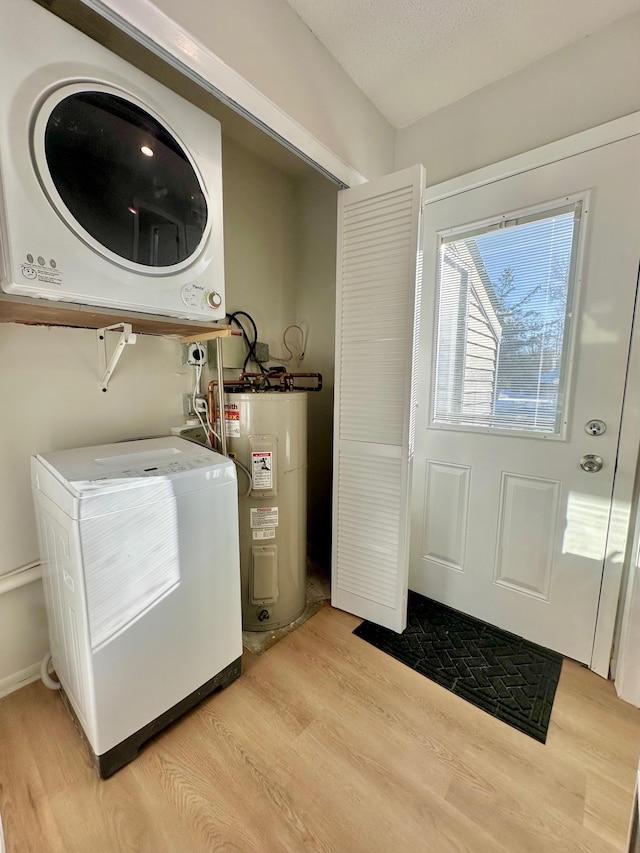 clothes washing area with stacked washer / drying machine, light hardwood / wood-style flooring, electric water heater, and a textured ceiling