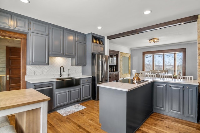 kitchen with stainless steel appliances, a peninsula, a sink, tasteful backsplash, and gray cabinets