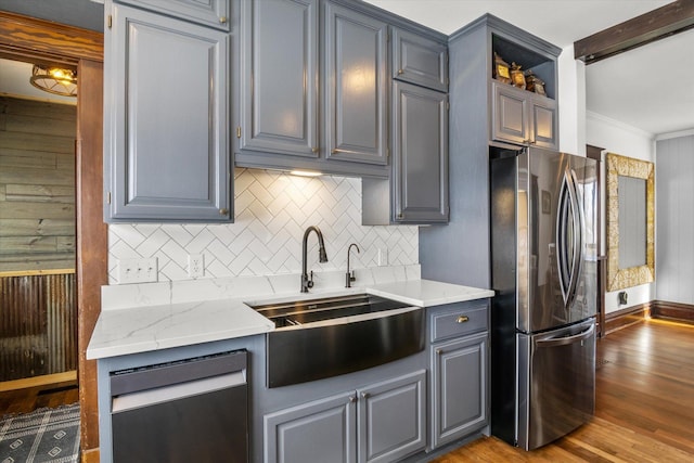 kitchen featuring wood finished floors, a sink, gray cabinets, stainless steel appliances, and backsplash