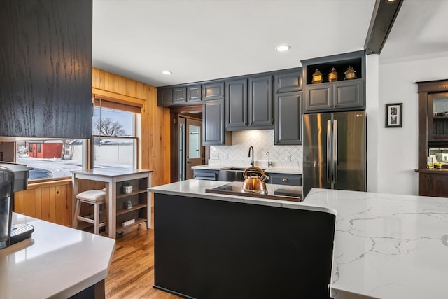 kitchen with light wood finished floors, backsplash, a sink, freestanding refrigerator, and light stone countertops
