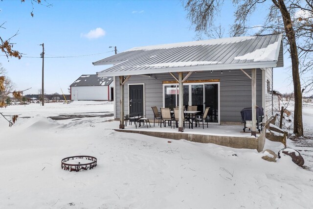 snow covered back of property with a patio and metal roof