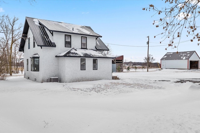 view of snowy exterior with metal roof, central air condition unit, and stucco siding