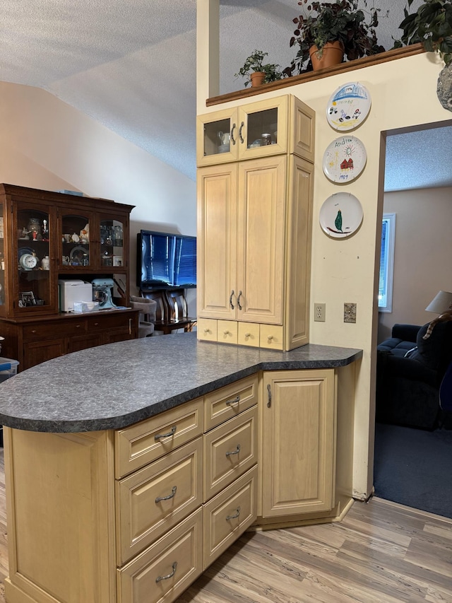 kitchen featuring lofted ceiling, light brown cabinetry, light hardwood / wood-style flooring, and a textured ceiling