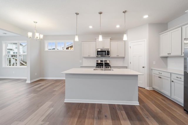 kitchen with pendant lighting, white cabinetry, stainless steel appliances, and a center island with sink