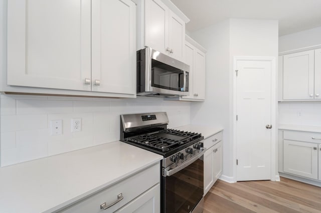 kitchen with tasteful backsplash, white cabinetry, appliances with stainless steel finishes, and light hardwood / wood-style flooring