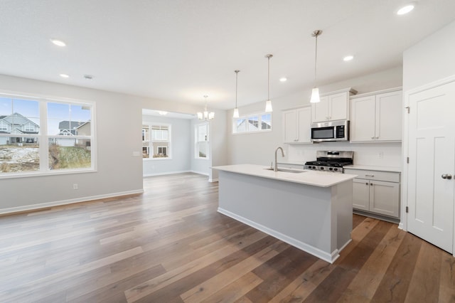 kitchen featuring appliances with stainless steel finishes, decorative light fixtures, white cabinetry, an island with sink, and sink