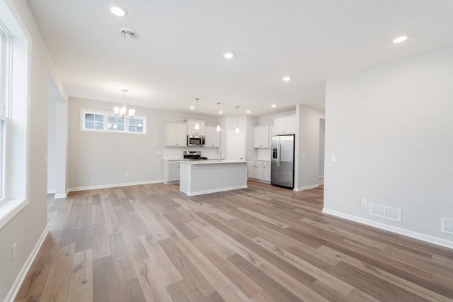 unfurnished living room featuring an inviting chandelier and light hardwood / wood-style floors