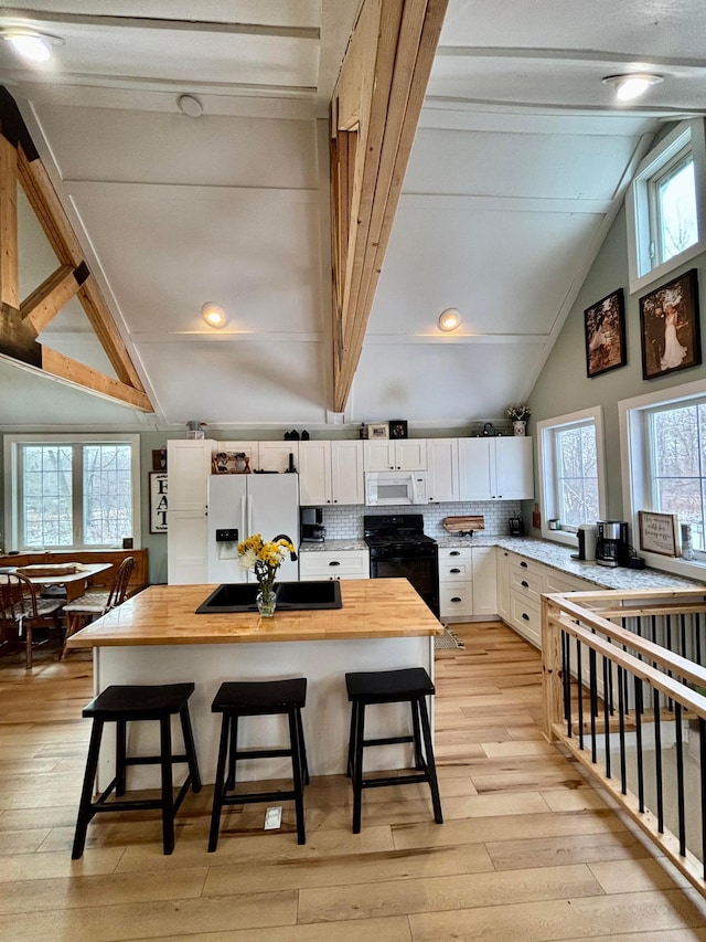 kitchen featuring white cabinetry, tasteful backsplash, wooden counters, a kitchen breakfast bar, and white appliances