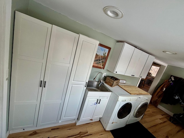 laundry area with light hardwood / wood-style flooring, sink, washer and clothes dryer, and cabinets