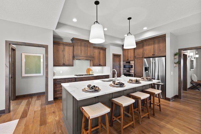 kitchen with pendant lighting, an island with sink, sink, light hardwood / wood-style floors, and stainless steel appliances