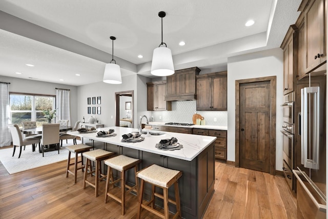 kitchen featuring sink, hanging light fixtures, light hardwood / wood-style flooring, stainless steel appliances, and a kitchen island with sink