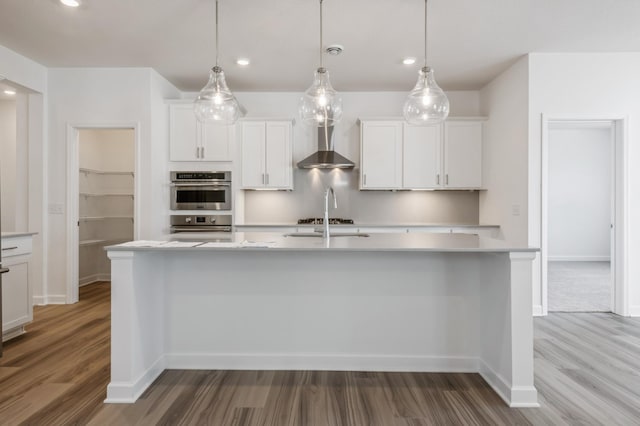 kitchen featuring hanging light fixtures, an island with sink, white cabinetry, and wall chimney exhaust hood