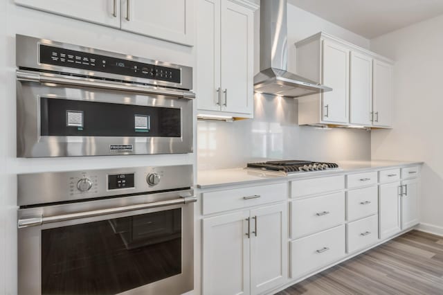 kitchen featuring white cabinetry, appliances with stainless steel finishes, wall chimney exhaust hood, and light hardwood / wood-style flooring