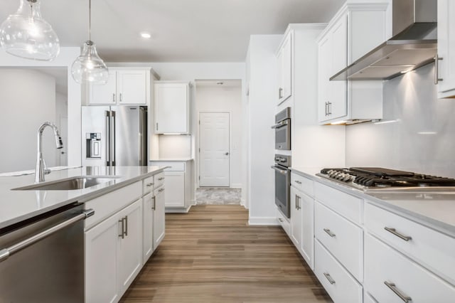 kitchen featuring sink, white cabinetry, hanging light fixtures, appliances with stainless steel finishes, and wall chimney range hood