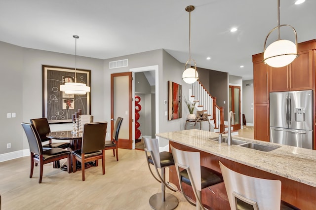 kitchen with stainless steel refrigerator with ice dispenser, light stone countertops, sink, and pendant lighting