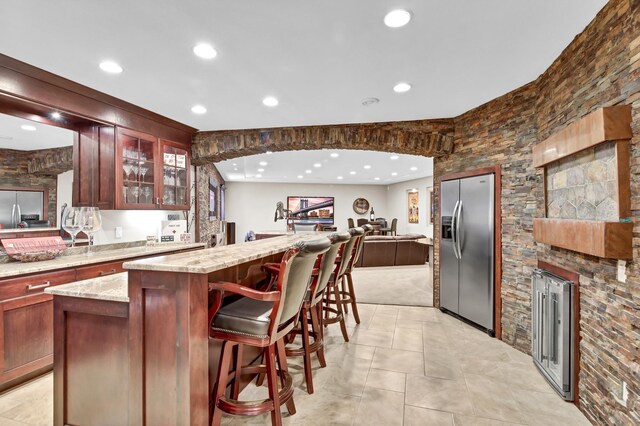 kitchen featuring a kitchen bar, light stone counters, stainless steel fridge with ice dispenser, built in fridge, and a kitchen island