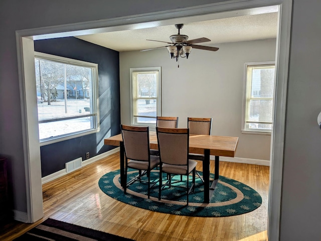 dining room with visible vents, a textured ceiling, wood finished floors, baseboards, and ceiling fan