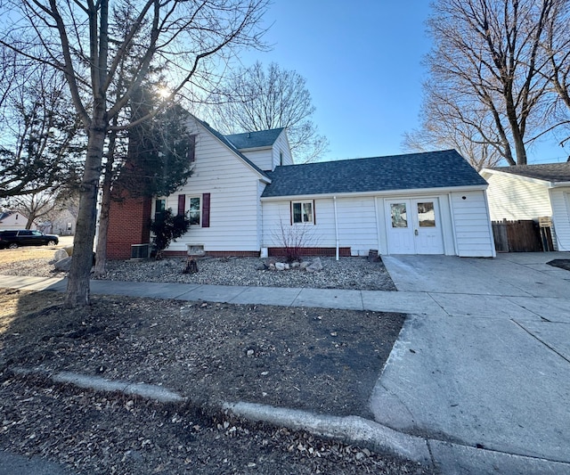 view of front of house with fence, central AC unit, concrete driveway, and a shingled roof