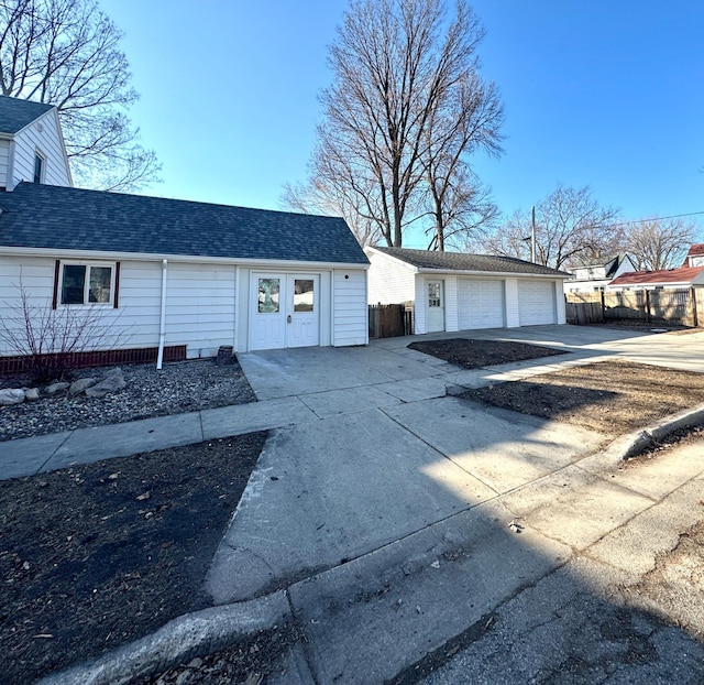 exterior space featuring an outbuilding, fence, a garage, and a shingled roof