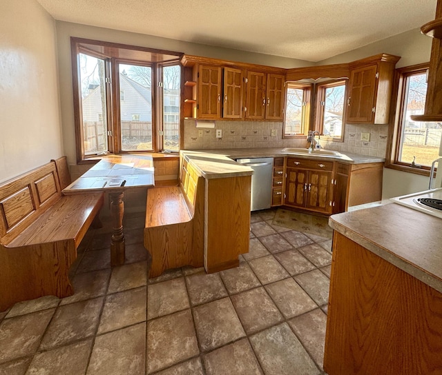 kitchen featuring brown cabinetry, decorative backsplash, dishwasher, and a sink