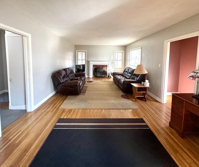 living area with a fireplace, a textured ceiling, baseboards, and wood finished floors