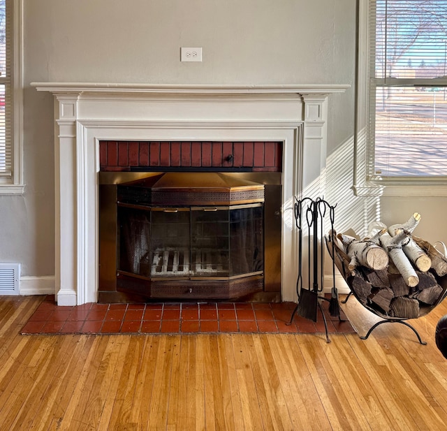 room details with visible vents, a fireplace with flush hearth, baseboards, and wood finished floors